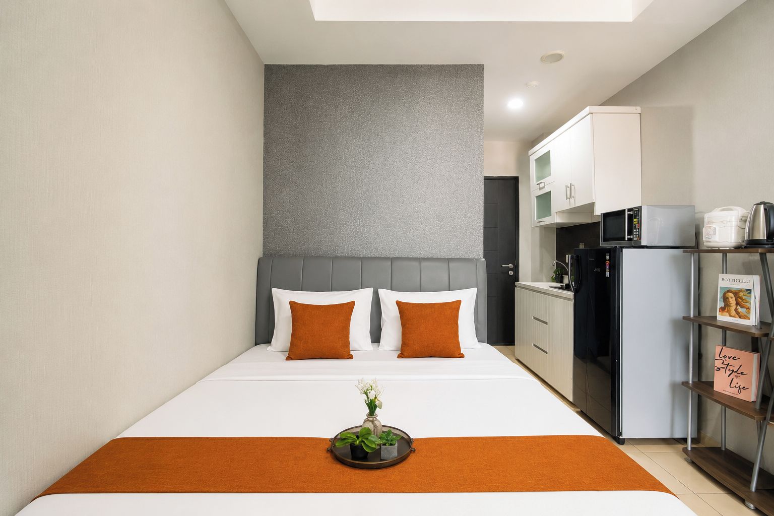 A compact hotel room with a bed, a small kitchen area, and a grey textured wall.