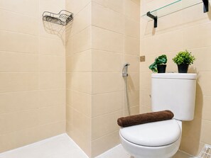 Ein Badezimmer mit einer weißen Toilette, einer Dusche und einem Handtuch auf der Sitzfläche. Auf dem Toilettentank stehen zwei Blumentöpfe.