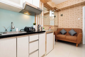 A modern kitchen with a built-in stove, a sink, and a range hood. There is a brown sofa with cushions in the adjacent living area. - Classic Comfortable 1Br At Apartment Green Pramuka City (Jakarta)