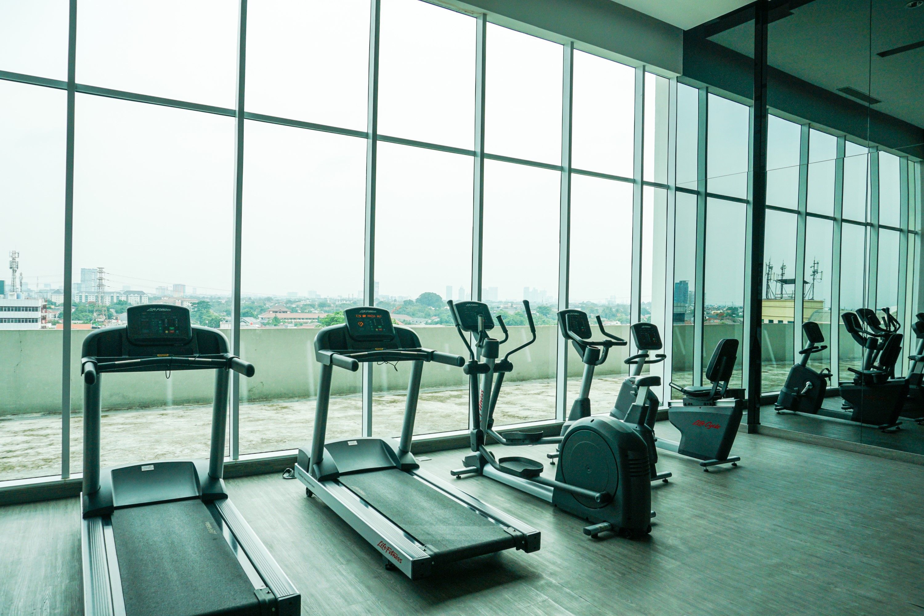 Ein Fitnessstudio mit Laufbändern, Crosstrainern und Fahrrädern, ausgestattet mit großen Fenstern und Blick auf die Stadt.