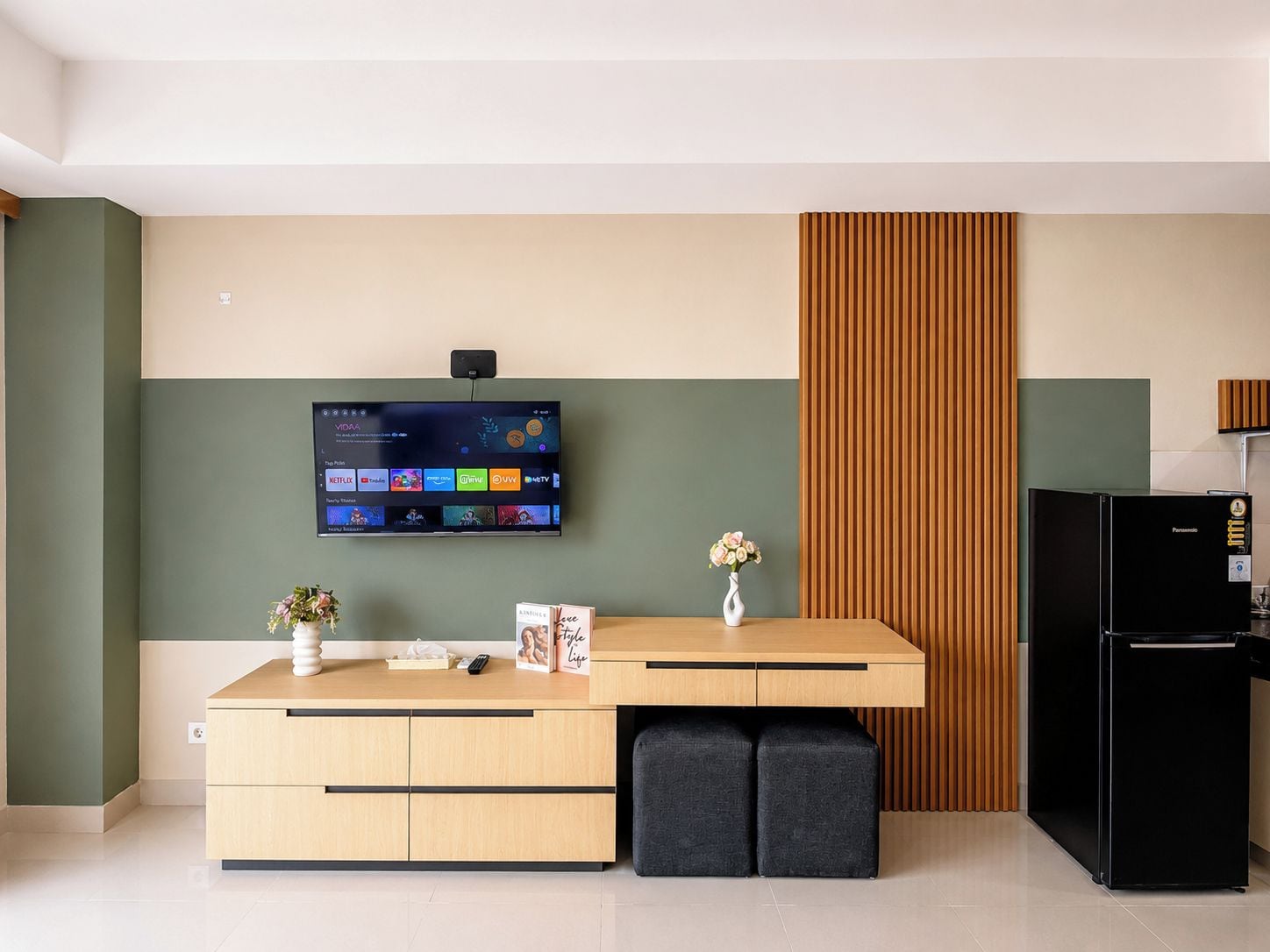 Una cuina moderna amb un televisor de pantalla plana al mur, un taulell de fusta, un refrigerador negre i un armari de fusta amb calaixos.