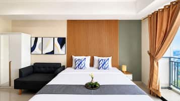 A hotel room with a large bed, a sofa, a wardrobe, and a view of the city.