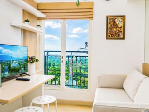 A modern living room with a balcony, a television, and a painting. - Bright And Comfy 2Br Apartment Podomoro Golf View (Depok)