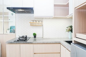 A modern kitchen with a gas stove, a black range hood, and a hexagonal tile backsplash. - Bright And Comfy 2Br Apartment Podomoro Golf View (Depok)