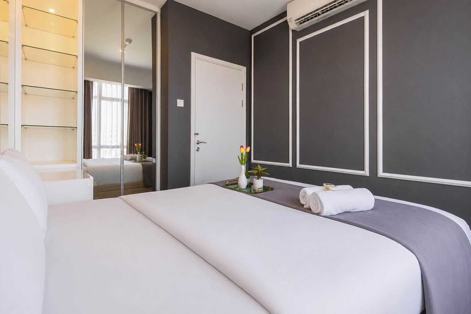 A hotel room with a bed, a bedside table with a vase of flowers, a mirror, and a wardrobe.
