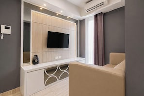 A modern living room with a flat-screen TV mounted on a wooden cabinet, a sofa, and a large window with curtains. - 2Br Apartment With Modern Design At Grand Sungkono Lagoon (Surabaya)