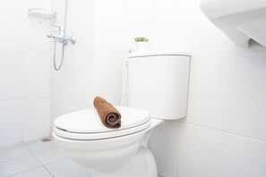 A white toilet with a towel on the seat, a showerhead, and a small plant on the wall. - Warm Relaxing Studio Room At Apartment Patraland Urbano (Bekasi)