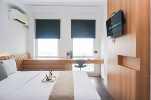 A hotel room with two beds, a desk, a TV, and a window with blinds. - Warm Relaxing Studio Room At Apartment Patraland Urbano (Bekasi)