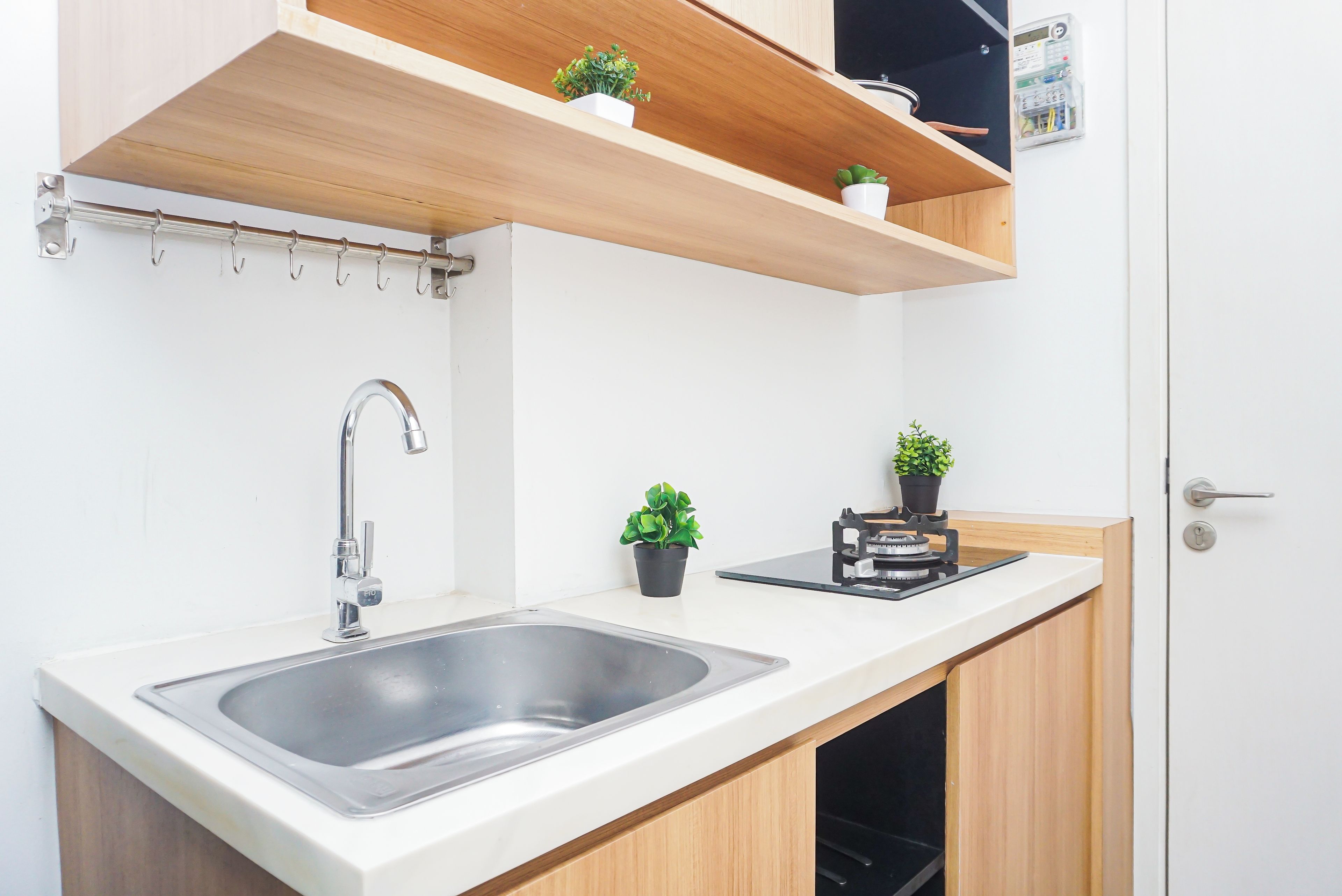 Cocina compacta con pileta de acero inoxidable, muebles de madera y una pequeña mesada con estufa incorporada.