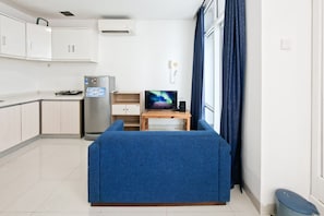 Ein kompakter Wohnraum mit Küchenzeile, einer Couch, einem Fernseher und einem Fenster mit Vorhängen.