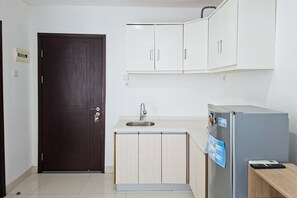 Eine kleine Küche mit einer dunkelholzigen Tür, einem Spülbecken, Schränken und einem Kühlschrank.
