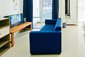 Ein modernes Wohnzimmer mit einem blauen Sofa, einem Holz-Fernsehschrank und einem großen Fenster mit Vorhängen.