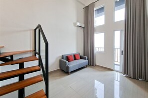 Un salon moderne avec un escalier, un canapé gris agrémenté de coussins rouges et de grandes fenêtres avec des rideaux.