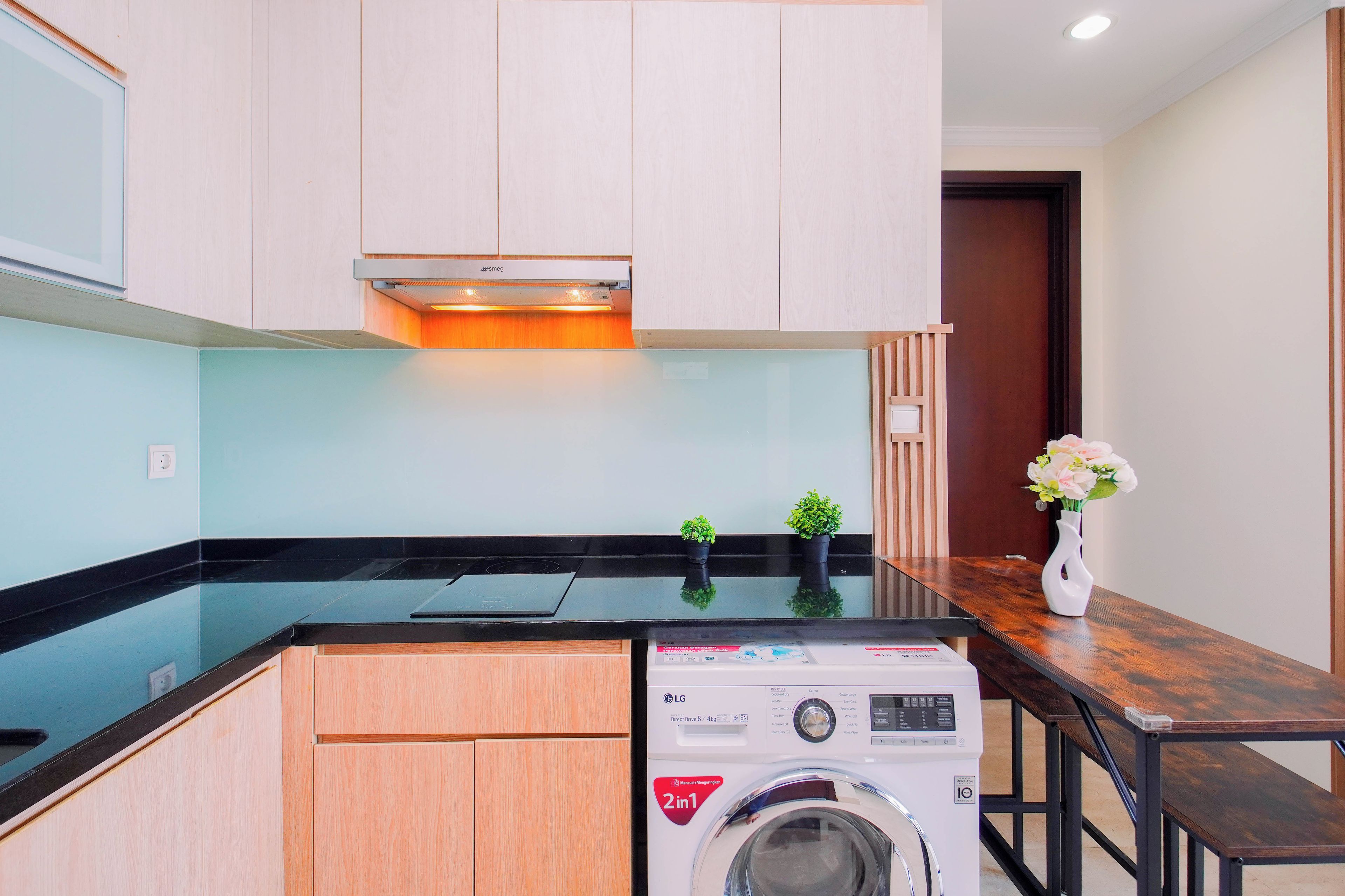 Cocina compacta con lavadora integrada, armarios de madera y una pequeña planta en maceta.