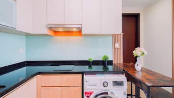 Cocina compacta con lavadora integrada, armarios de madera y una pequeña planta en maceta.