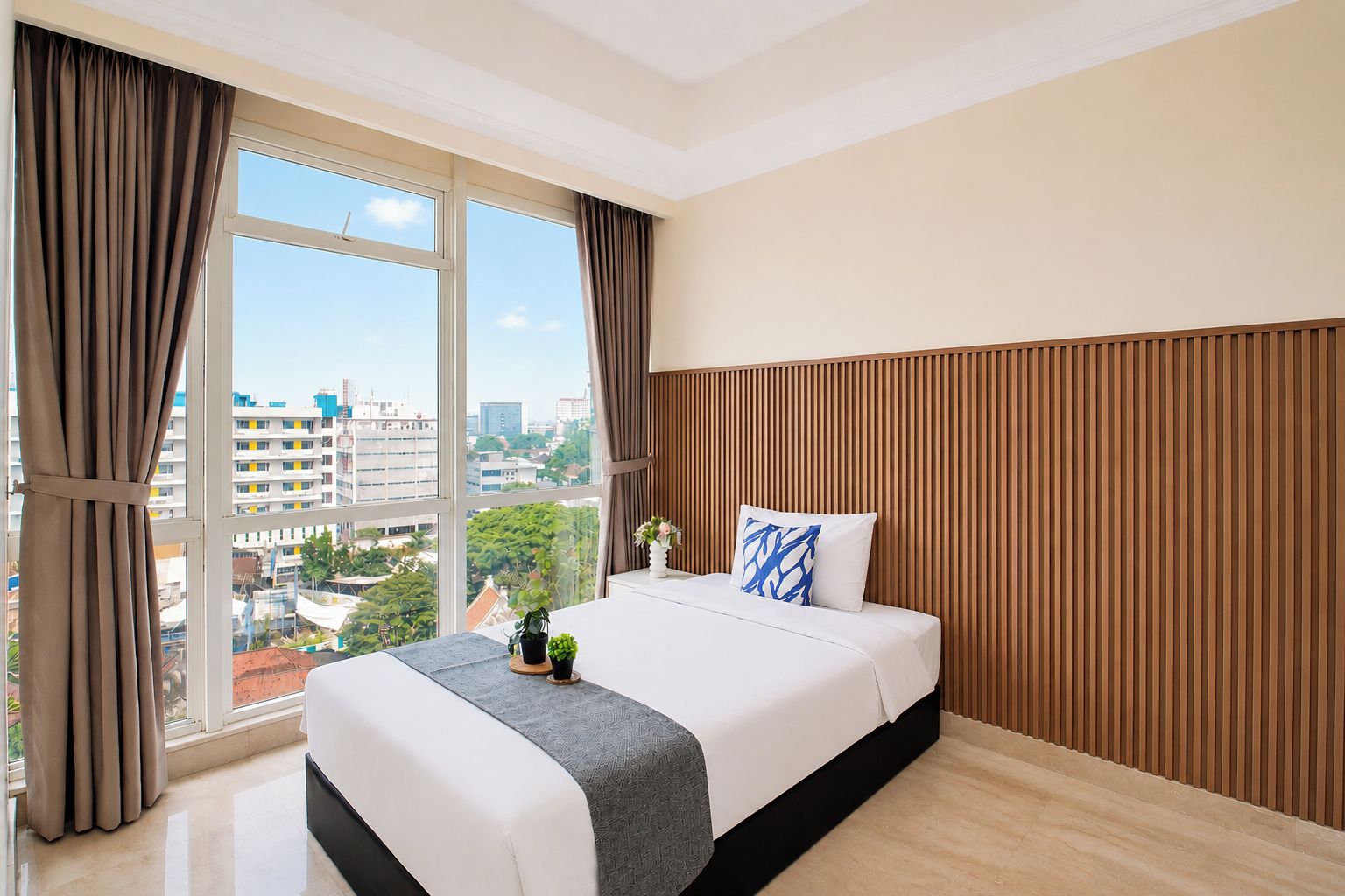 Una habitación de hotel con un ventanal grande, una cama con cubrecama gris y blanco, cabecera de madera con listones y vistas a la ciudad.