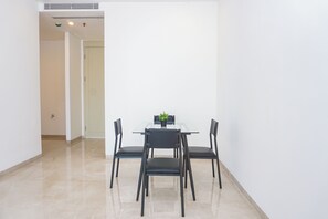 A minimalist room with a glass table and four chairs, a potted plant, and a door leading to another room. - Serene 1Br With Sky View At Apartment Izzara (Jakarta)