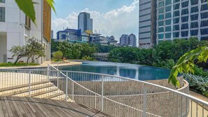 A rooftop pool with a wooden deck and a white railing, surrounded by greenery and modern buildings in the background. - Serene 1Br With Sky View At Apartment Izzara (Jakarta)