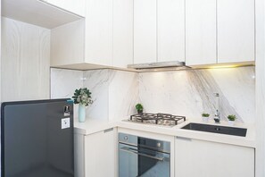 A modern kitchen with white cabinetry, a black refrigerator, a gas stove, and a built-in oven. - Serene 1Br With Sky View At Apartment Izzara (Jakarta)