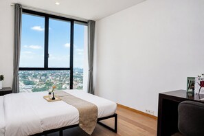 A hotel room with a large window, a bed, a desk, and a view of a cityscape. - Serene 1Br With Sky View At Apartment Izzara (Jakarta)