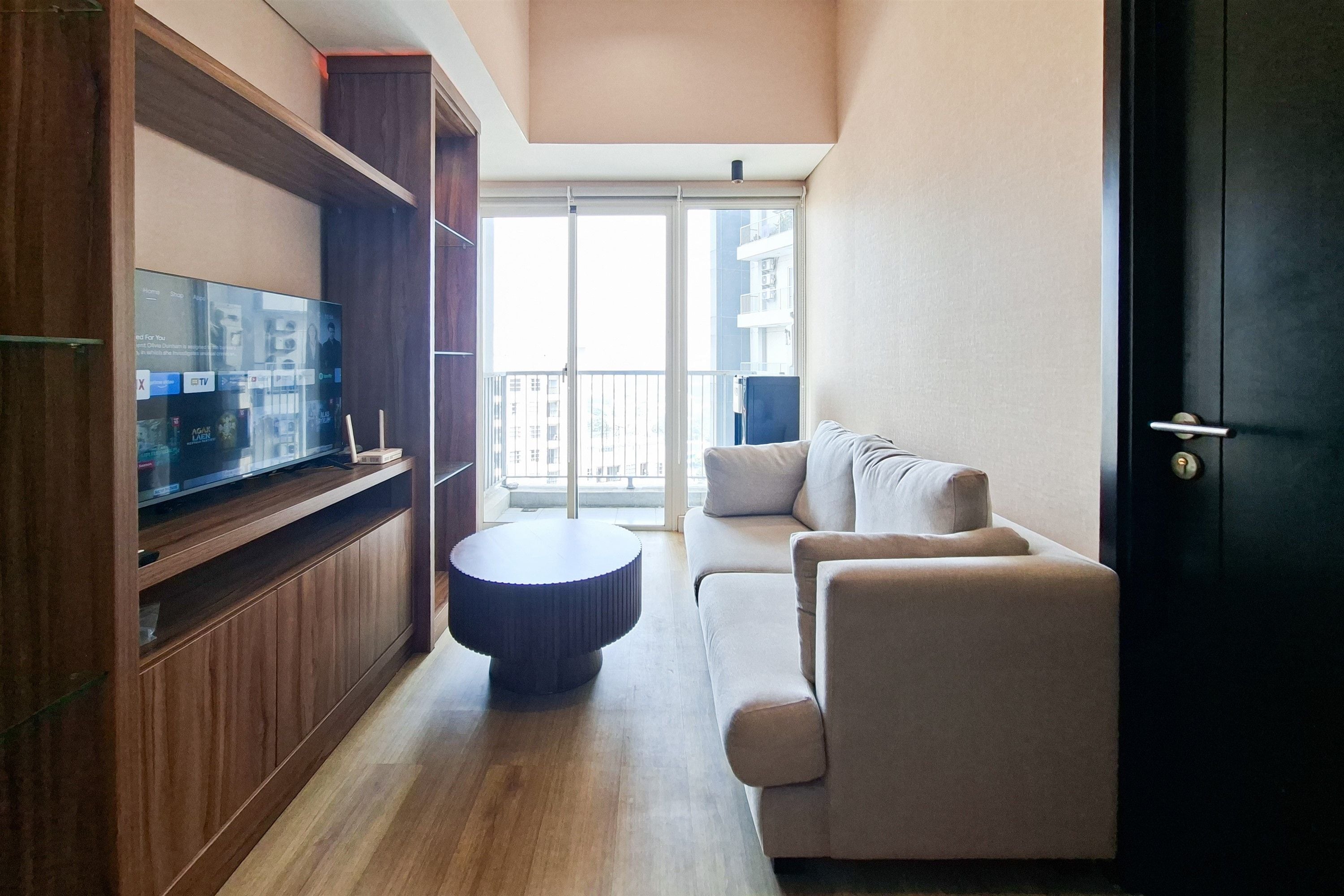 A modern living room with a flat-screen TV on a wooden stand, a round coffee table, and a sofa with cushions.