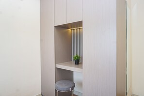 Ein kleiner, abgeschlossener Raum mit einer hellen Wand, einem Regal, einer Topfpflanze und einem Hocker.