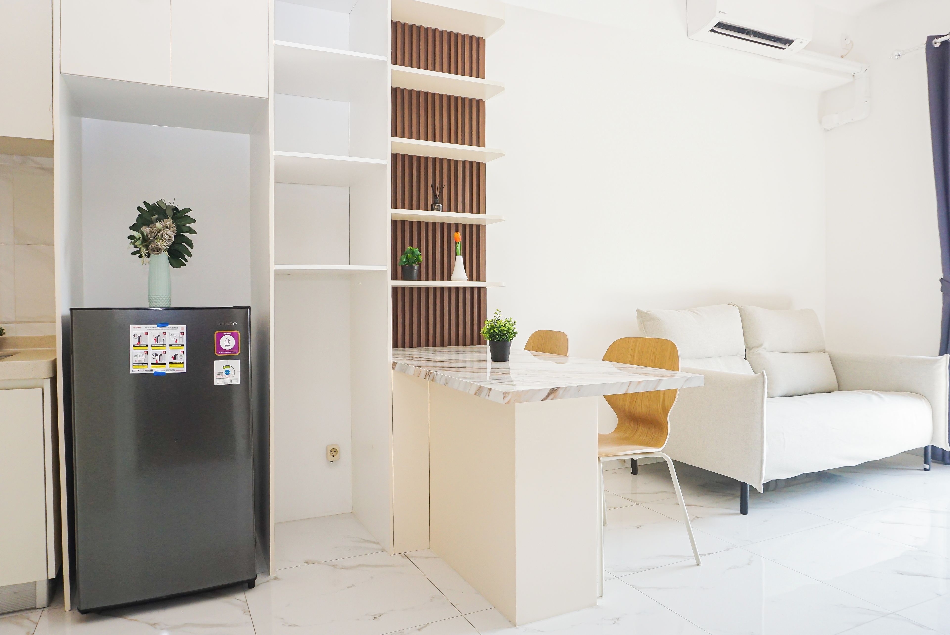 Cozinha moderna com geladeira embutida, área de jantar com mesa de mármore e sofá branco.