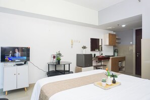 Ein modernes Hotelzimmer mit einem Bett, einem Fernseher, einem kleinen Tisch mit einer Vase und einer Küchenzeile.