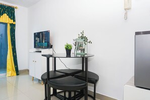 Ein kompakter Wohnbereich mit Küchenzeile, einem Esstisch mit zwei Stühlen, einer kleinen Topfpflanze und einem flachbildfernseher an der Wand.
