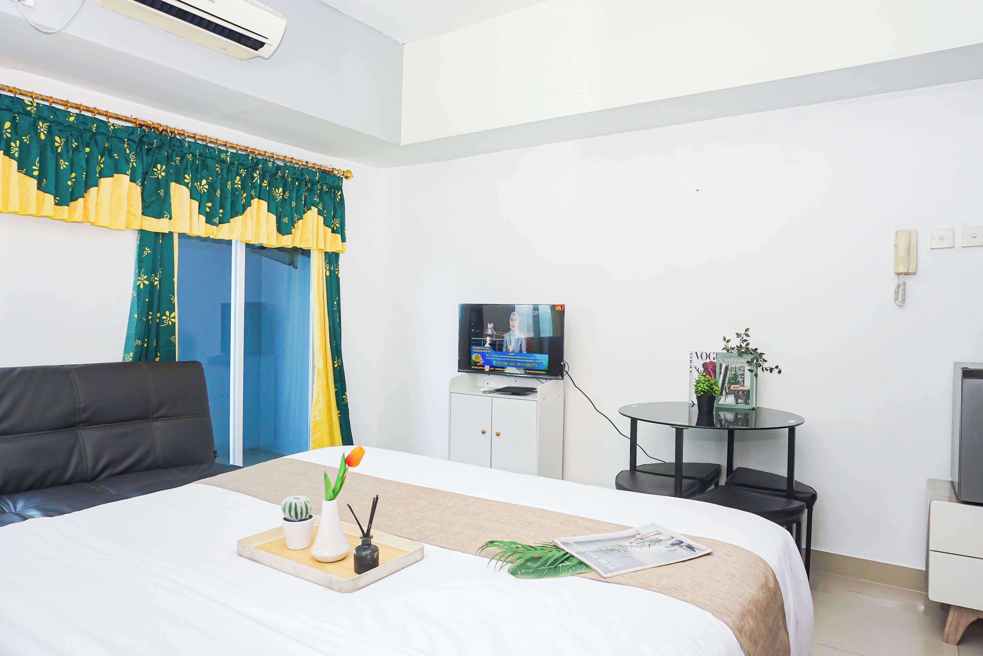A hotel room with a bed, a desk, a television, and a small table with a plant.