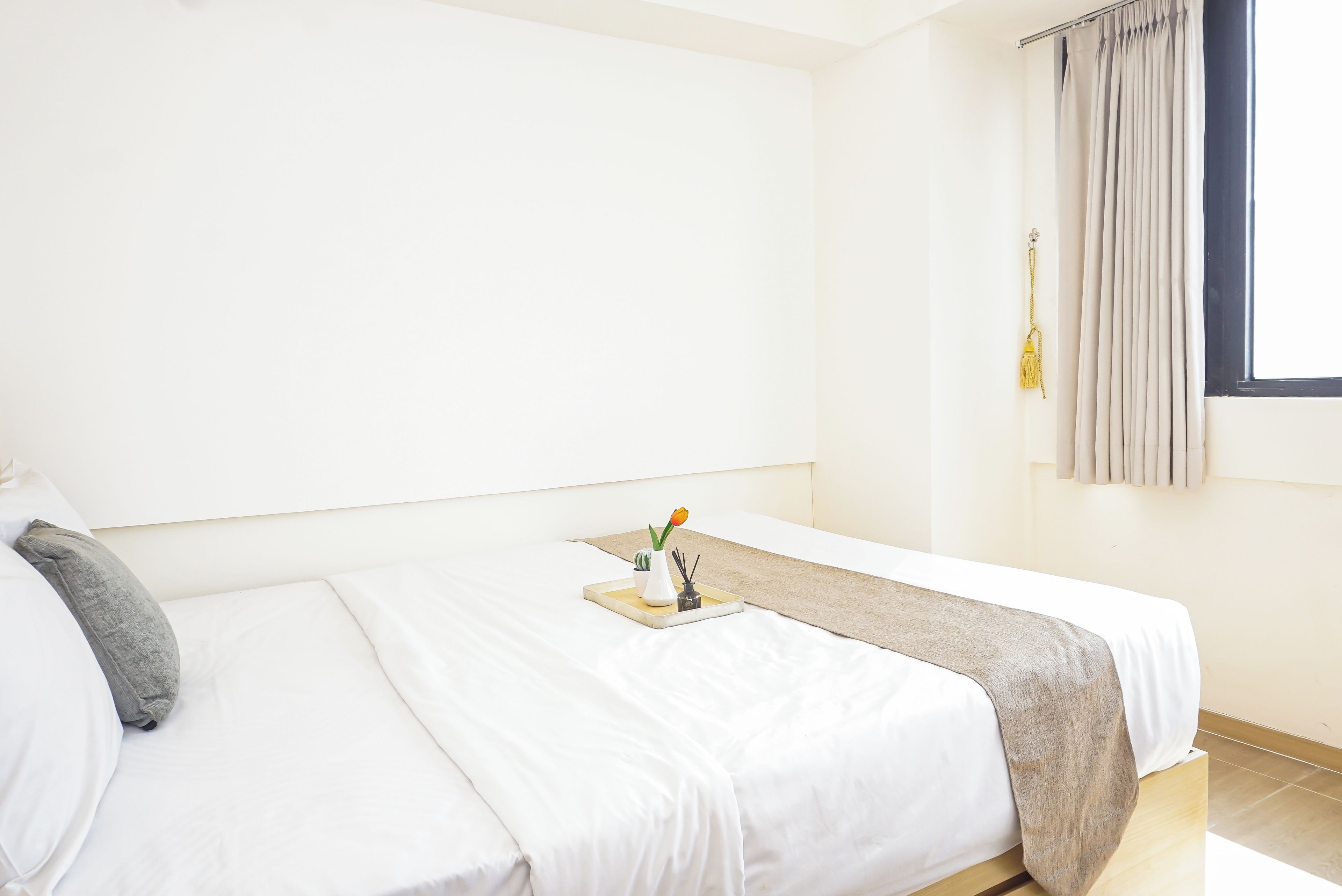 Habitación de hotel con dos camas individuales, una mesita con un florero y una vela, y un ventanal con cortinas.