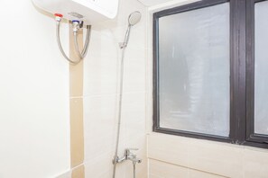 A shower with a handheld showerhead and a wall-mounted faucet, a window with a dark frame, and beige tiled walls. - Bright And Homey 2Br At Apartment Meikarta District 1 (Cikarang)