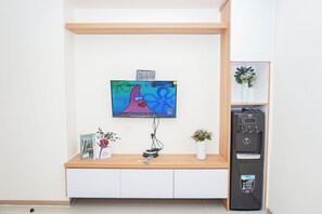A TV mounted on a wall with a wooden shelf below. - Warm And Restful 2Br At Apartment Meikarta District 1 (Cikarang)
