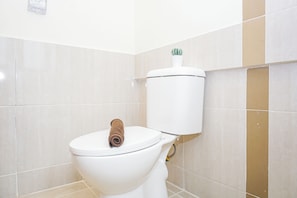 A white toilet with a towel on the seat and a toothbrush on the tank. - Warm And Restful 2Br At Apartment Meikarta District 1 (Cikarang)