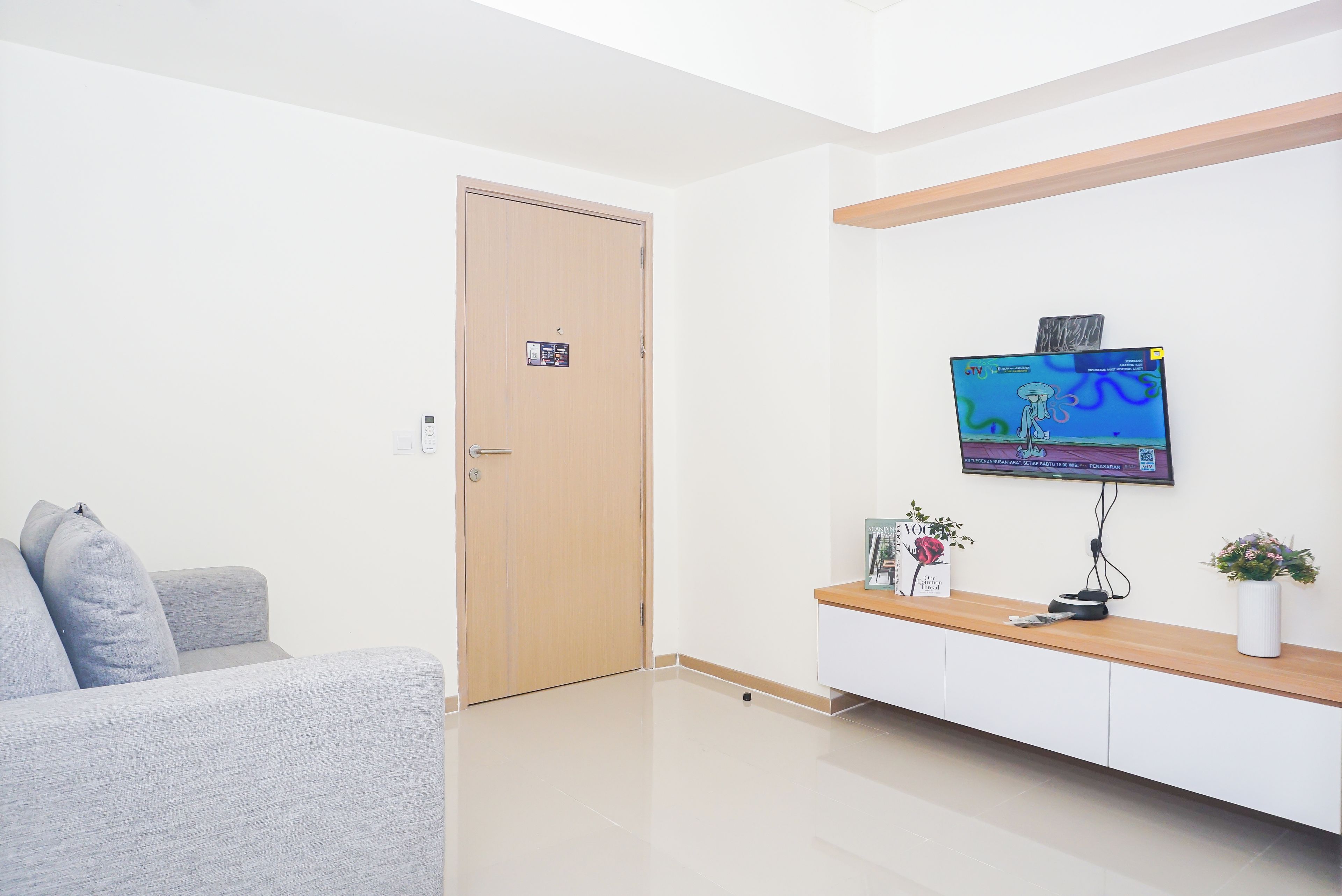 Un soggiorno moderno con una TV a schermo piatto montata a parete, un tavolino consolle in legno con un vaso e un divano grigio.