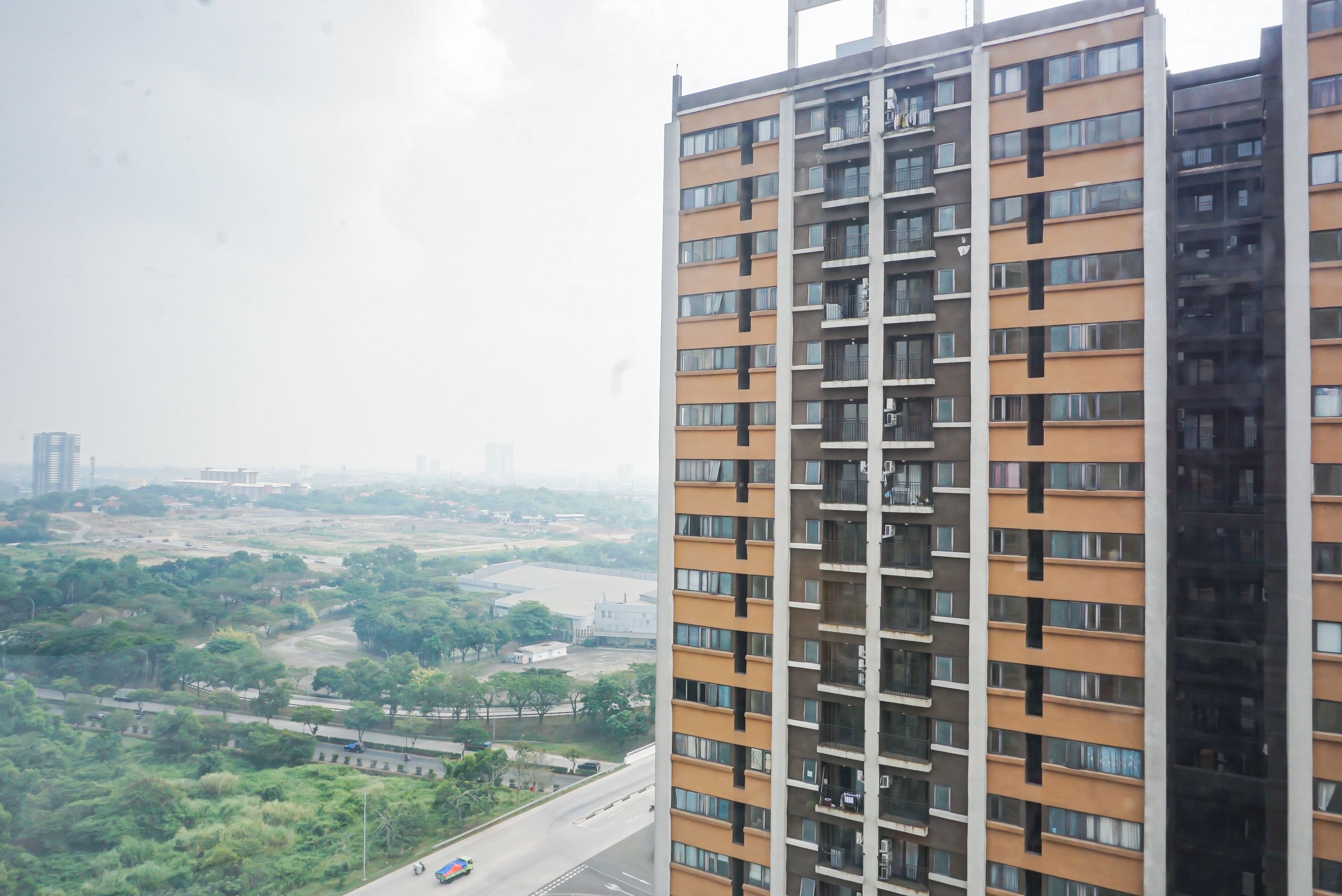 Un edificio alto con numerosi balconi, vista su una strada e vegetazione circostante.