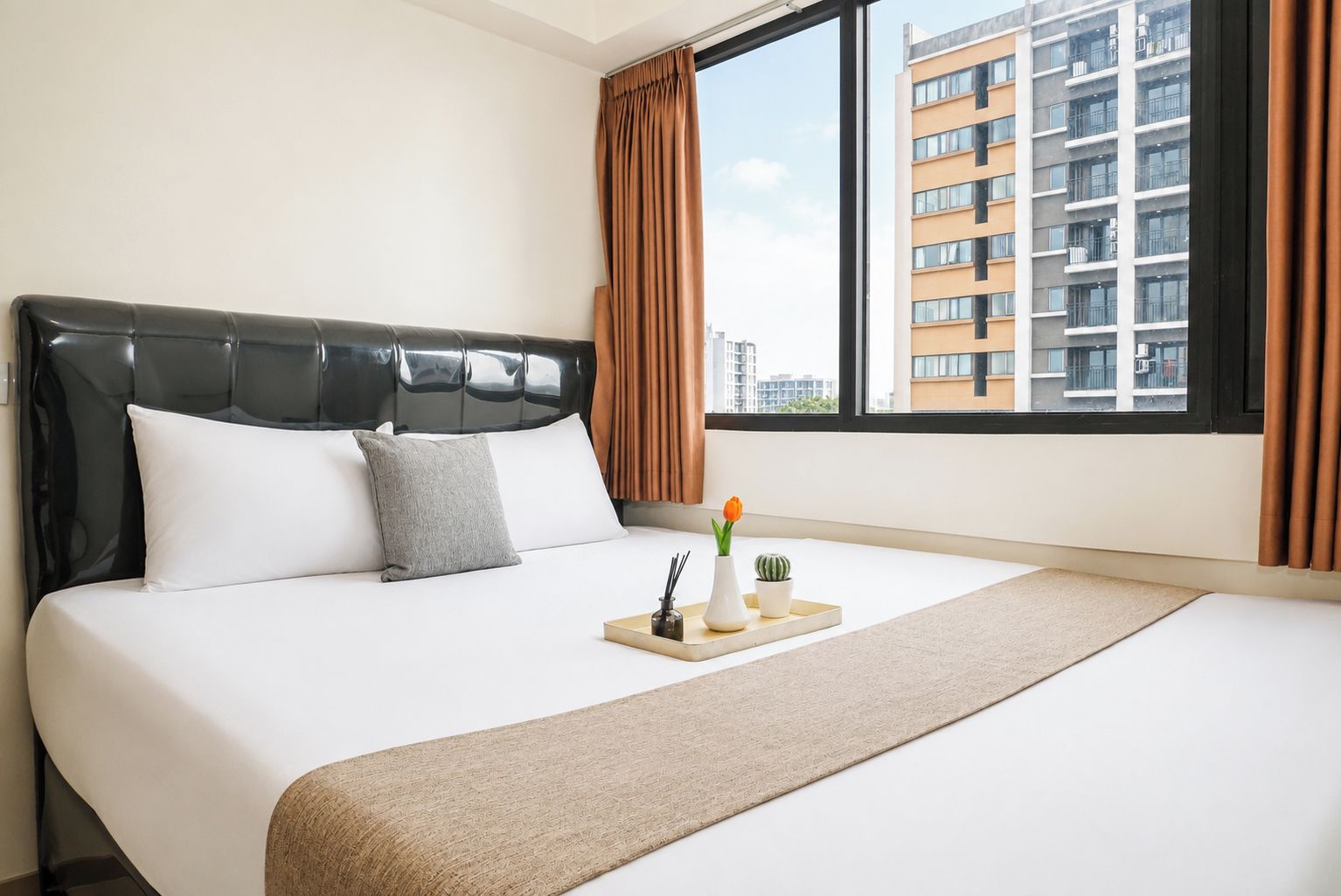 Una camera d'albergo con un letto grande, una testiera, una finestra con tende e vista su un edificio.