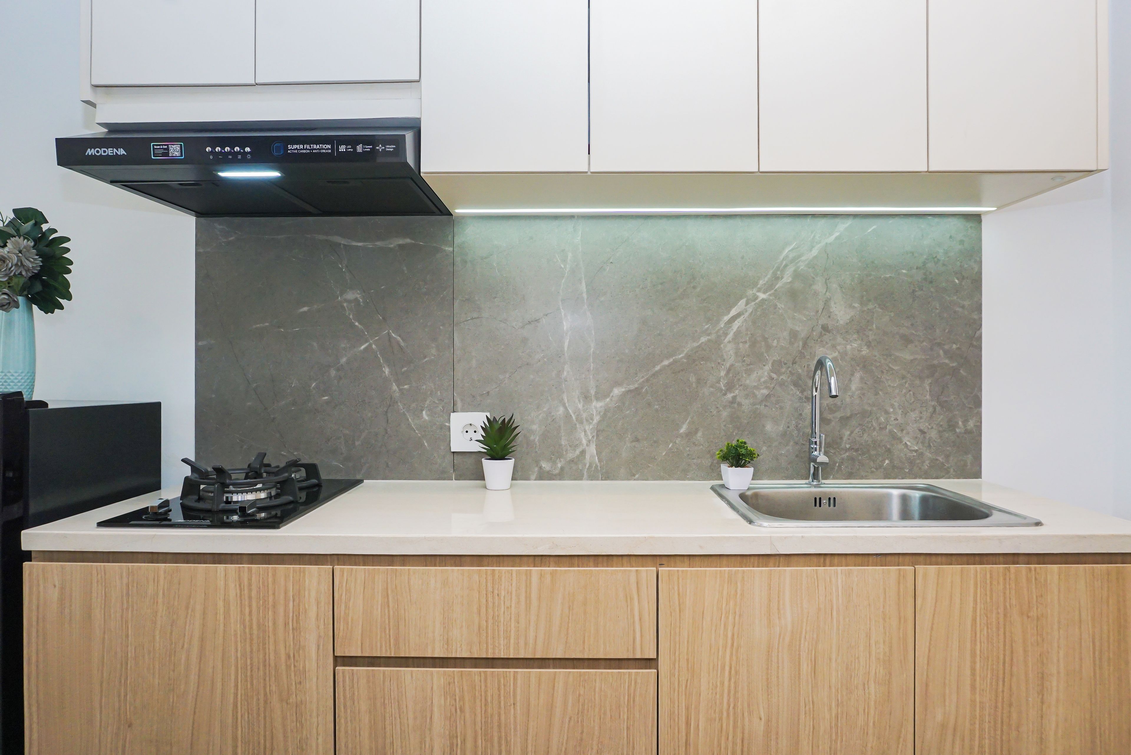 A modern kitchen with a gas stove, a stainless steel sink, and a marble backsplash.