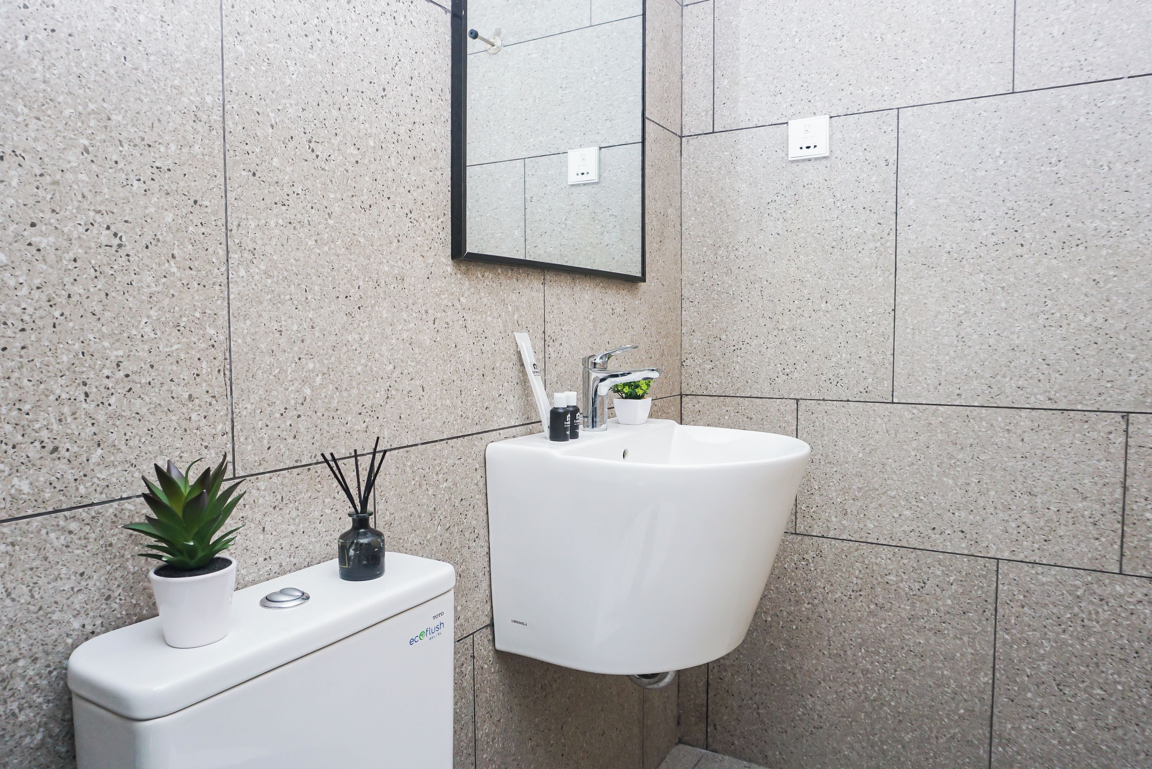 A bathroom with a white sink, a mirror, a potted plant, and a toilet.