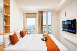 Ein Hotelzimmer mit Bett, Wandfernseher, Fenster mit Stadtblick und Balkon.