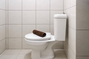 Eine weiße Toilette mit einem braunen Handtuch auf dem Sitz, vor einer gefliesten Wand.