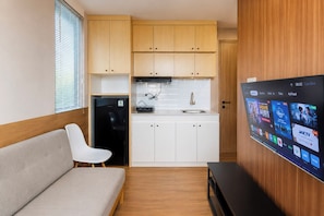 Eine kleine Küchenzeile mit Kühlschrank, Spüle und Holzschränken. Ein Flachbildfernseher an der Wand zeigt verschiedene Sender.