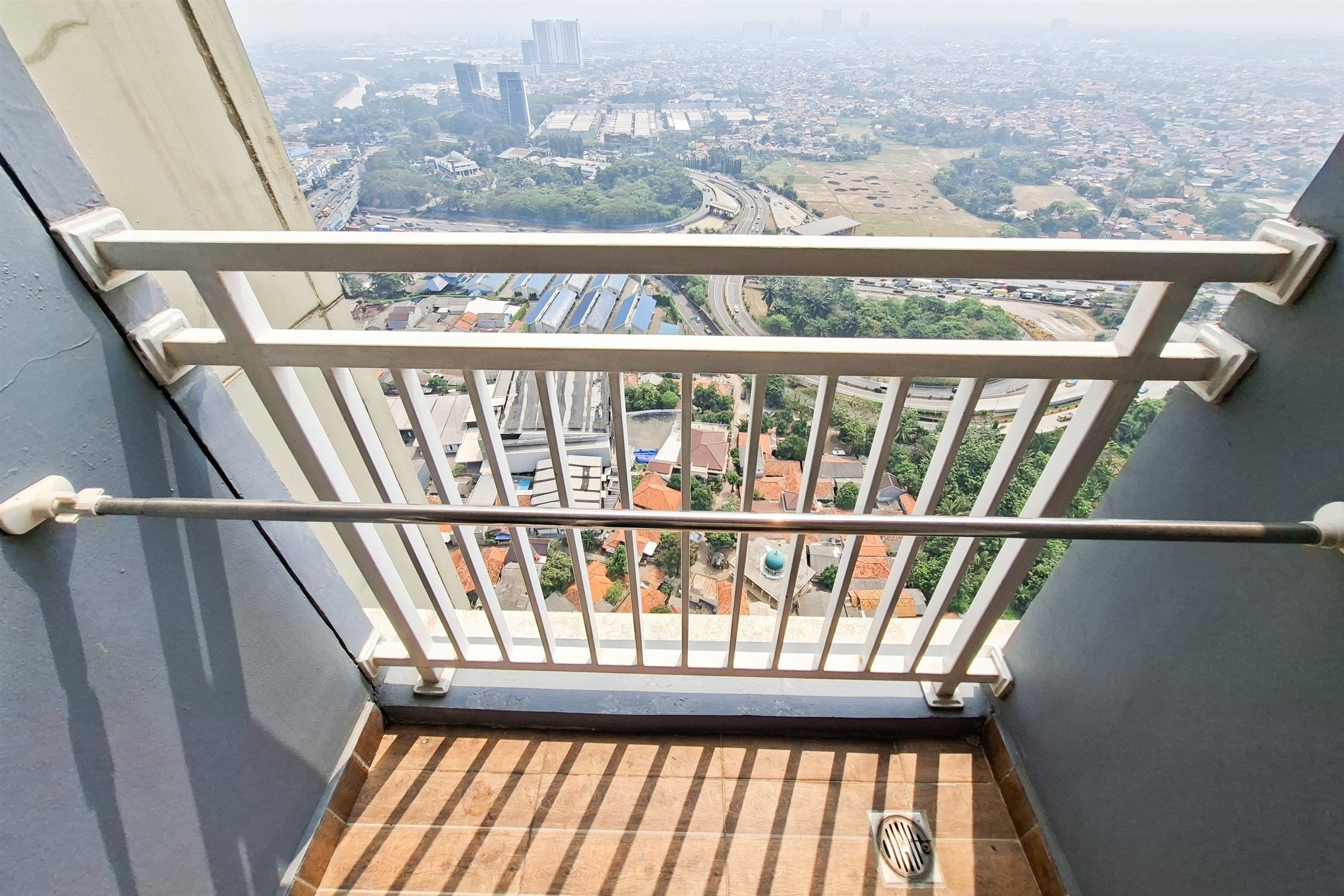 Un balcón con barandilla metálica que da a una vista panorámica de la ciudad, con edificios y calles.