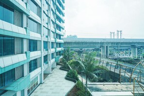 A modern building with multiple floors, large windows, and a central courtyard with greenery. - Functional And Cozy Studio At Apartment Grand Kamala Lagoon (Bekasi)