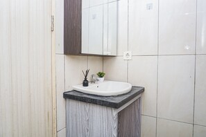 A bathroom with a white sink, a mirror, a small potted plant, and a black marble countertop. - Functional And Cozy Studio At Apartment Grand Kamala Lagoon (Bekasi)