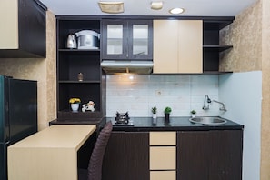 A compact kitchen with dark cabinetry, a built-in stove, a sink, and a small countertop area. - Functional And Cozy Studio At Apartment Grand Kamala Lagoon (Bekasi)