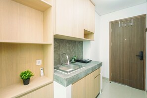 A modern kitchen with a built-in sink, a small potted plant, and a wooden door. - Minimalist Studio At Apartment B Residence Grogol (Jakarta)
