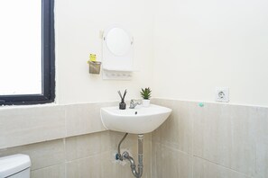 Ein Badezimmer mit einem weißen Waschbecken, einem Spiegel, einer kleinen Topfpflanze und einer Toilette.