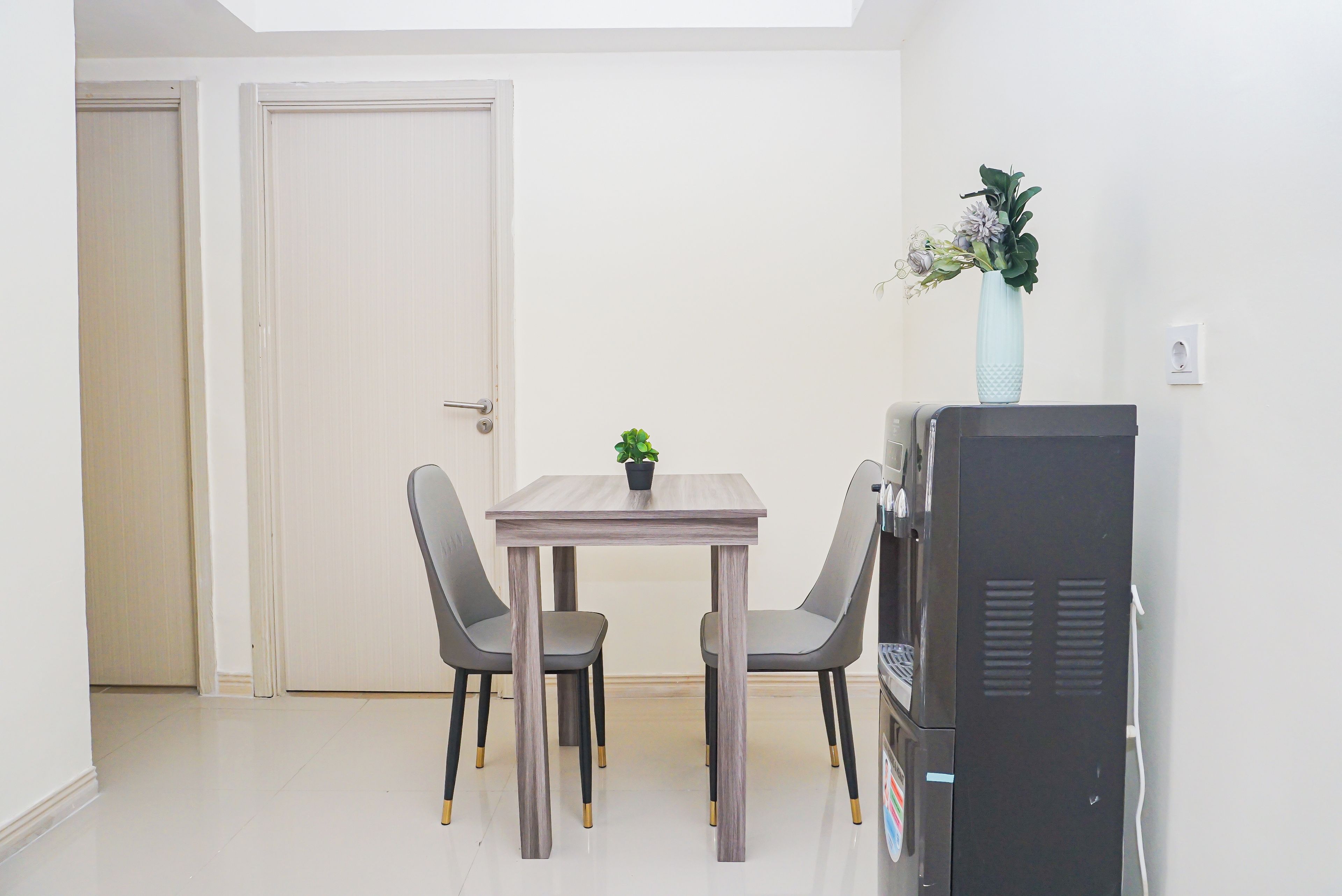 Un petit coin repas avec une table et deux chaises, une plante en pot et un téléviseur posé sur un meuble.