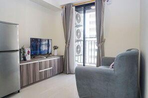 Un salon moderne doté d’un téléviseur à écran plat, d’un canapé gris, d’un réfrigérateur encastré et d’un balcon avec vue.